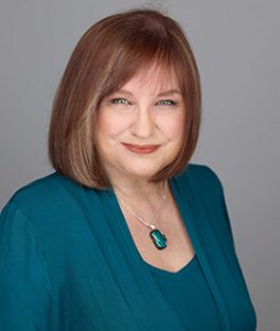 Photo of Laurel Parsons who has auburn hair and is wearing a turquoise blouse with a necklace featuring a pendant of the same colour.